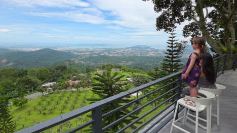little girl standing on the chair beside her mother admiring the beautiful views in summer. - wide shot