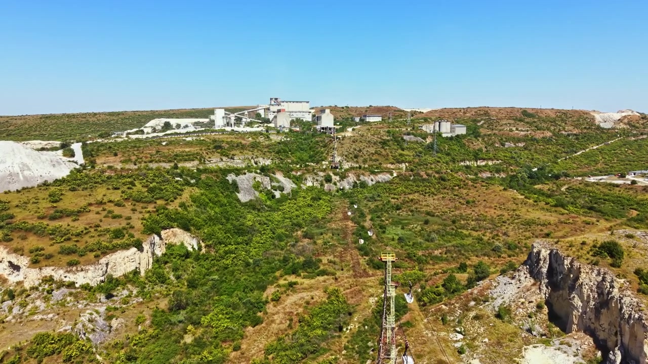 Vista di un sito industriale immerso nel verde su una collina sotto un cielo azzurro e sereno di giorno