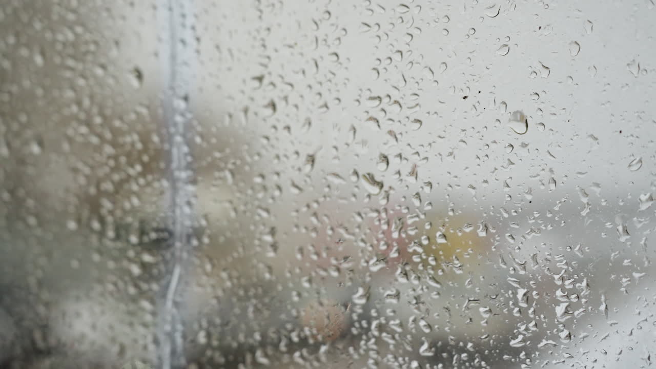 Rainsoaked streets and blurred traffic. Moist glass with moving vehicle shadows. Faint motion and reflections on wet urban windowpane. Dewy window capturing slowmoving cars and muted cityscape hues