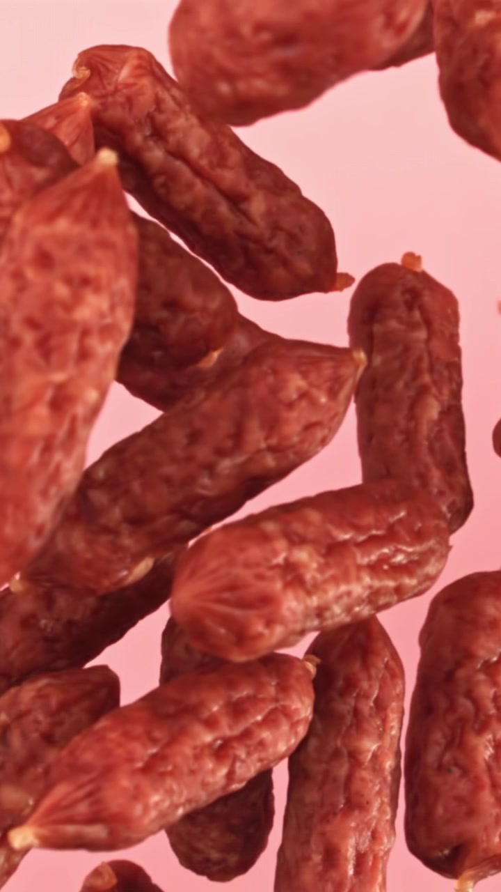 Primo piano di mini salamini che galleggiano su sfondo rosa