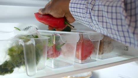 una persona abre un refrigerador para revelar una variedad de verduras frescas organizadas en contenedores.