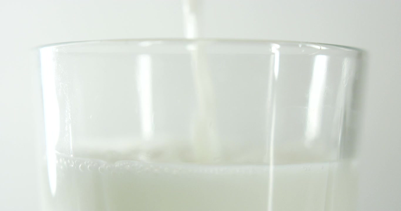 susu yang sedang dituang dan hanya menunjukkan bagian atas gelas dengan latar belakang putih bersih