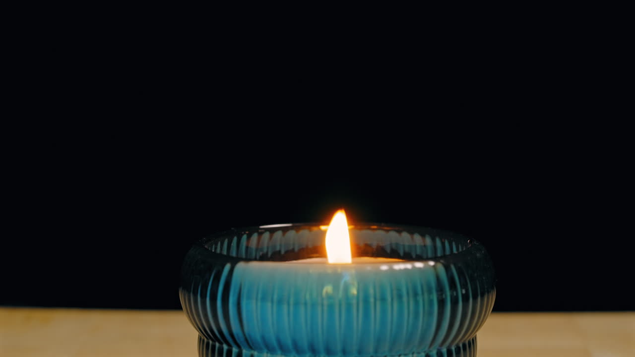 Piccola candela in un contenitore di vetro soffiata più volte e finalmente spenta su uno sfondo nero.
