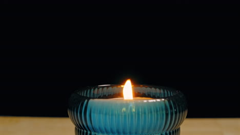 small candle in glass container blown multiple times and finally extinguished against a black backdrop