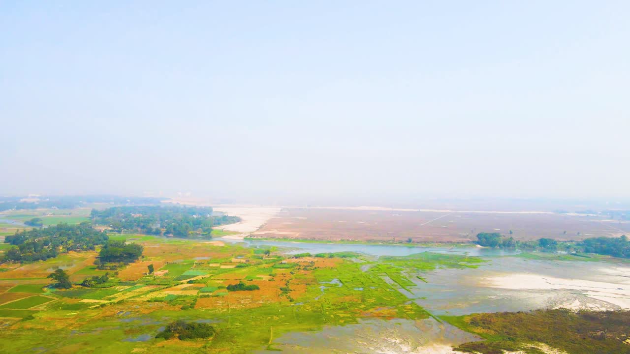 Rising aerial view over fresh village farms irrigated with water during summer season. 4K