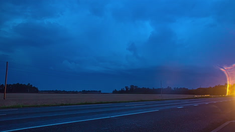 toma de tiempo de autos conduciendo por la carretera a lo largo del paisaje rural con relámpagos visibles en el fondo a lo largo de la nube oscura moviéndose en el cielo nocturno