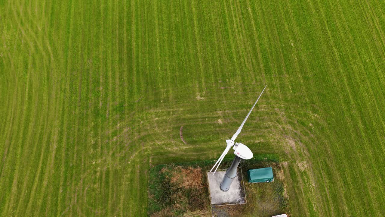 Overhead drone footage captures a single wind turbine spinning in a lush green agricultural field near Kinross, Scotland, under natural daylight