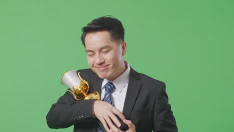 close up of asian business man in a suit and tie with a gold medal hugging a gold trophy being proud winning as the first winner on green screen background in the studio