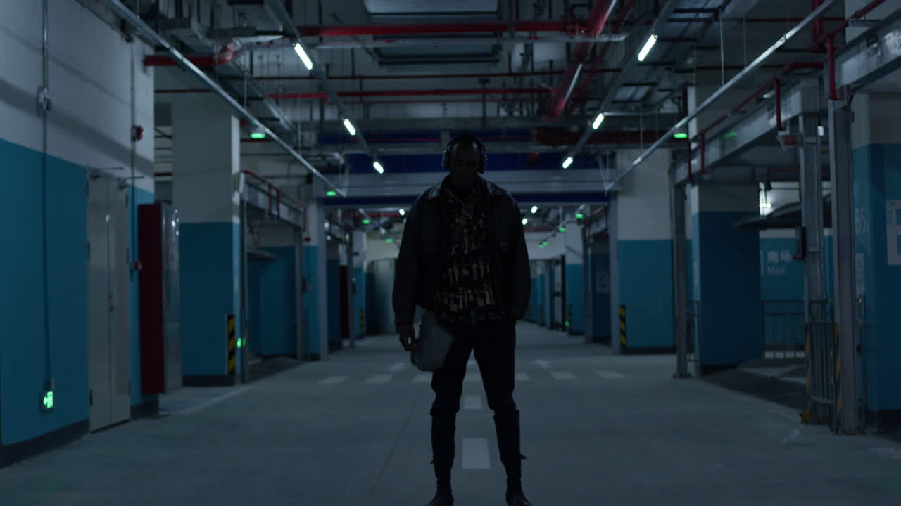 젊은 흑인 미국 래퍼가 지하 주차장 주차장에서 차갑고 조용히 서 있습니다.