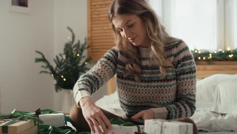Caucasian-woman-sitting-on-bed-and-packing-Christmas-gift-at-home