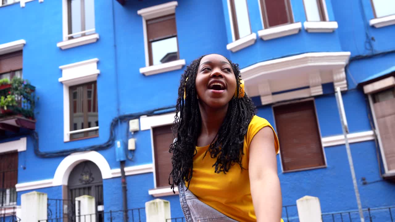 Young woman with headphones in front of blue building