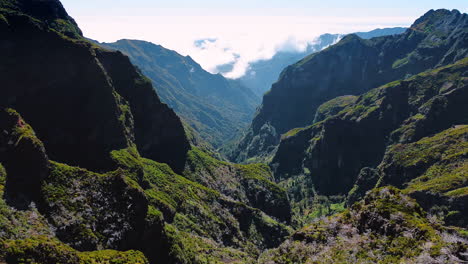 Dangerous rocks covered with mosses and lichens. Sunny view of mountains in Madeira, Portugal. White cloudscape spreading at backdrop.