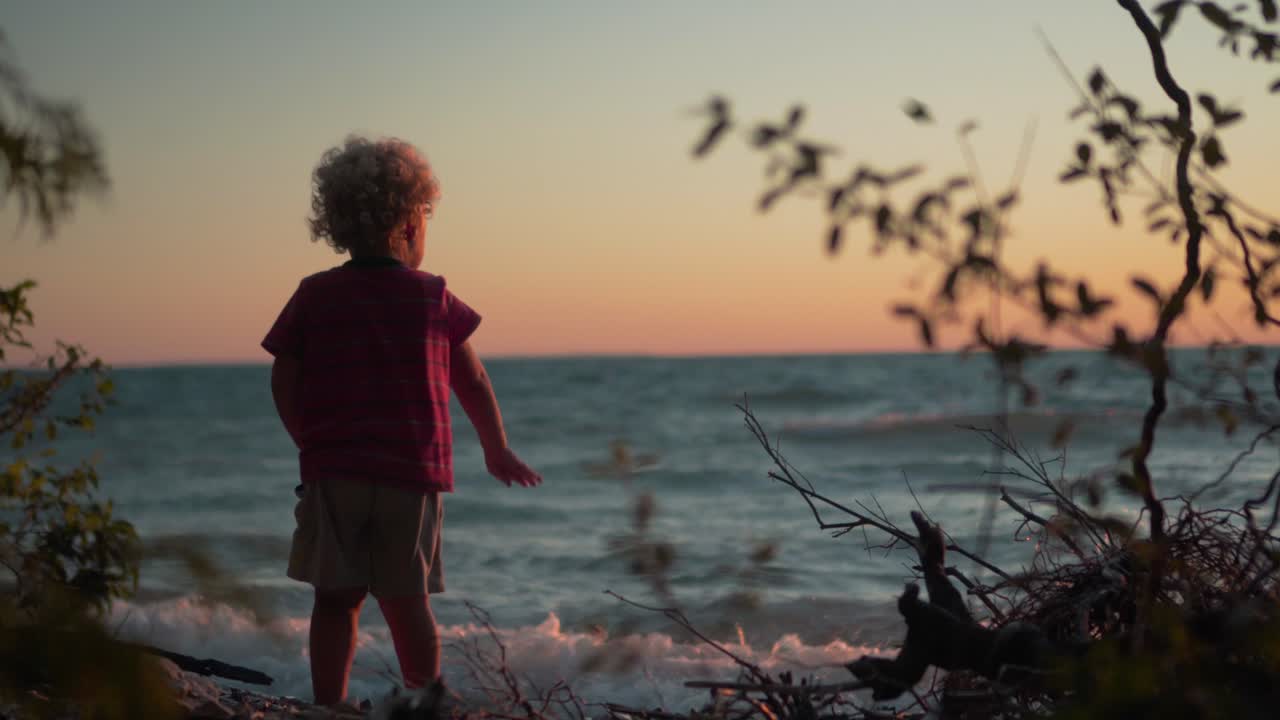 Silhouette Shot of Little Boy Throwing Rocks into the Water at the Beach During Sunset