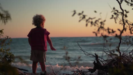 silhouette shot of little boy throwing rocks into the water at the beach during sunset