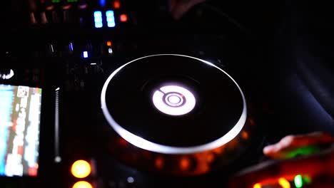 soft view of man hand disc jockey mixing and blending music tracks on his deck in the darkness of a party or night club