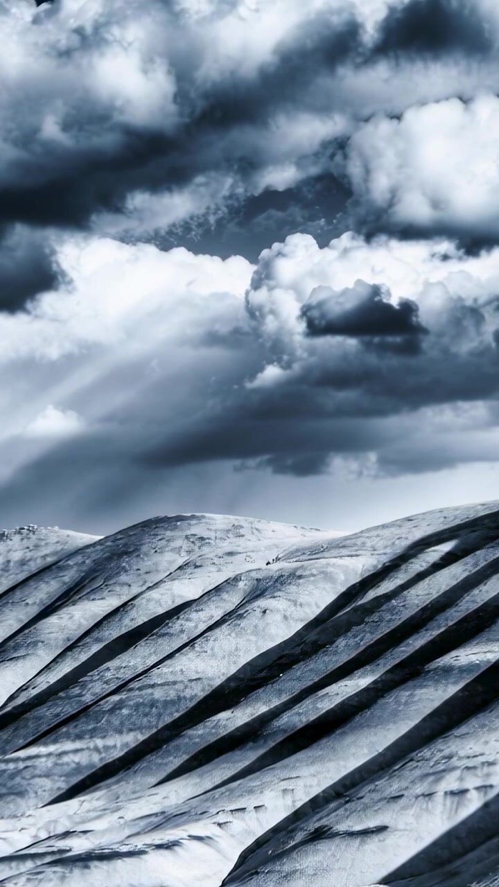 Vertical video: Shifting clouds casting light shafts, ridges receiving diagonal shadows on dunes
