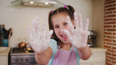 portrait of caucasian girl wearing apron with flour powder on her hands in the kitchen at home