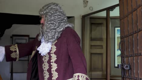 man in 18th-century attire walking through a castle hallway