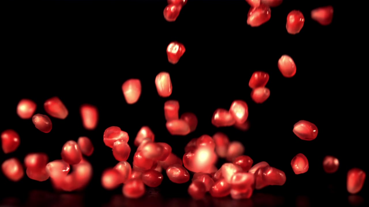 Red Pomegranate Seeds Falling in Slow Motion on Black Background