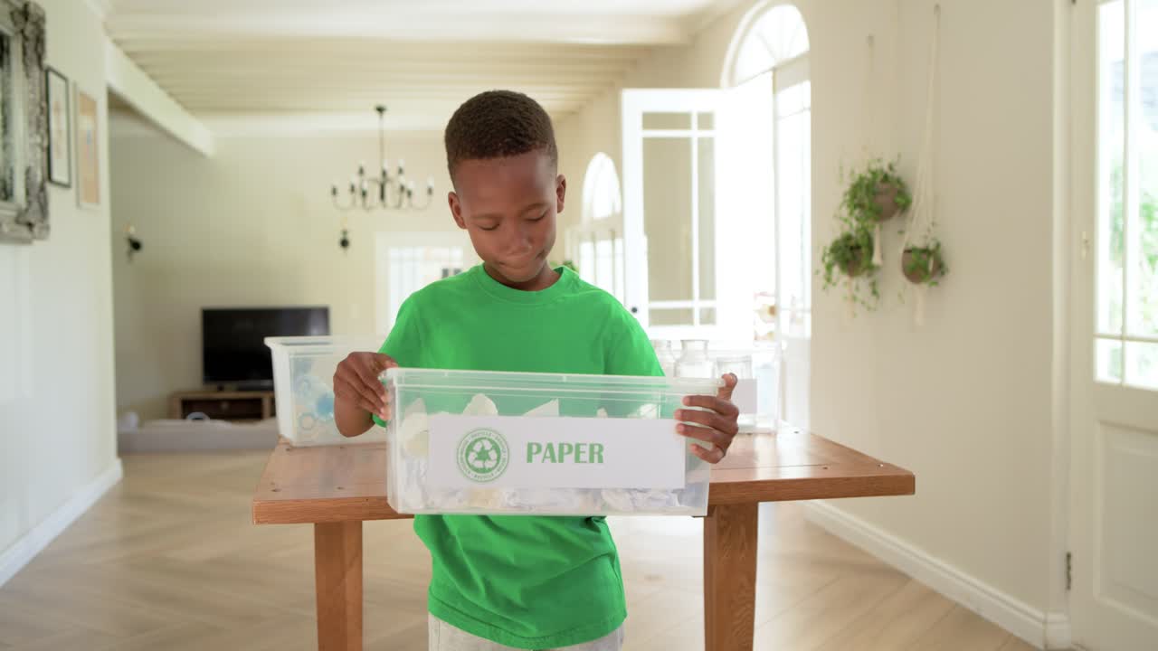 African American school age boy finding paper, placing it into PAPER bin to recycle at home