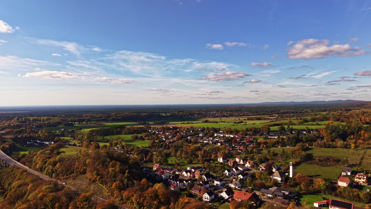 Colorful autumn landscape showcasing a peaceful village surrounded by vibrant foliage and rolling hills in the countryside during a clear afternoon
