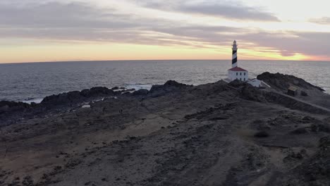 rocky trail leads people to the favartix lighthouse in spain with the sun setting in the background