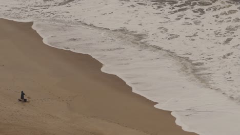 Sand-beach-with-one-person-in-Nazare,-Portugal,-sea-or-ocean-diagonal-composition