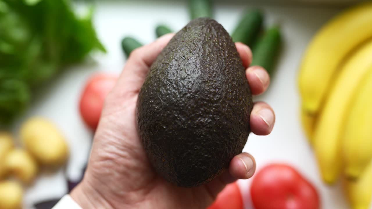 Mano che tiene un avocado con altri prodotti freschi