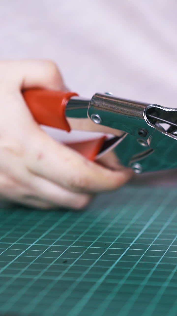 CU: Professional tailor makes holes in black leather strip with special punch pliers in workshop close view
