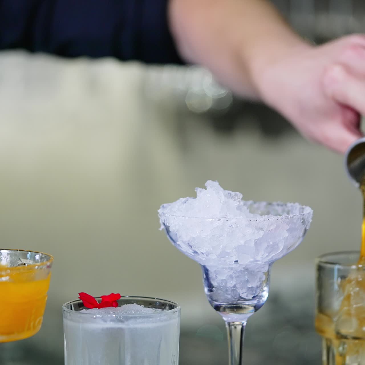 Diverse glasses with ice and liquid stuff. Unrecognized bartender filling the beaker with yellow liquid and pours it into glass. Blurred backdrop