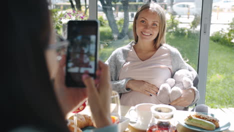 Pregnant woman being photographed by a friend in a cafe