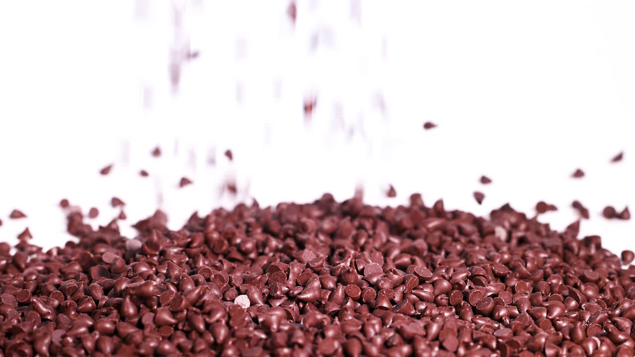 Chocolate pieces cascade onto a pile, set against a bright white background, creating a dynamic and visually appealing scene