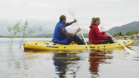 caucasian couple having a good time on a trip to the mountains, kayaking together on a lake