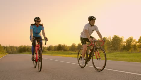 Two-professional-road-cyclists-ride-their-bikes-on-a-hill.-Hand-held-shot-of-two-strong-cyclists-female-and-male-on-their-training-on-a-warm-but-windy-summer-day