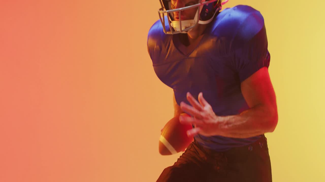 Video ravvicinato di un giocatore di football americano caucasico con casco e pallone su sfondo arancione.