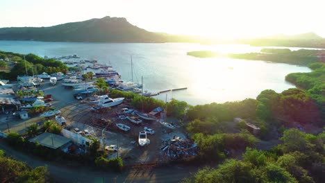 Golden-sunset-glow-spreads-across-water-of-piscadera-bay-inlet-with-yachts-in-dry-dock,-aerial