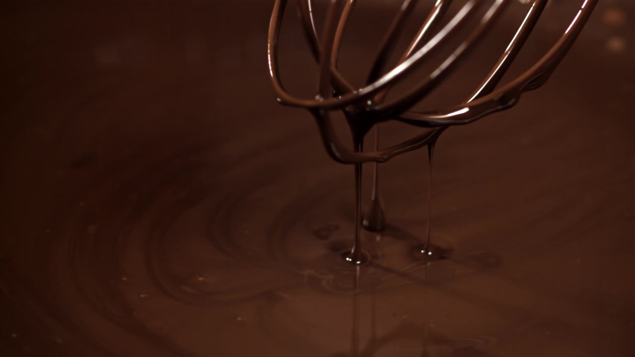 Ricco cioccolato fuso che cola da una frusta al rallentatore