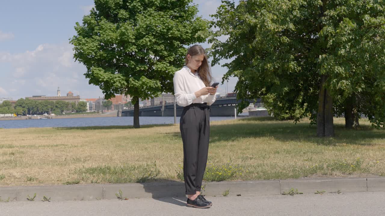 Geschäftsfrau tippt an einem strahlend sonnigen Tag im Park auf ihrem Smartphone.