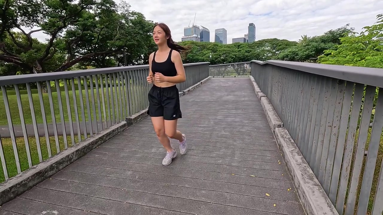 Una donna sportiva in abbigliamento nero corre su un ponte di cemento durante una giornata luminosa.