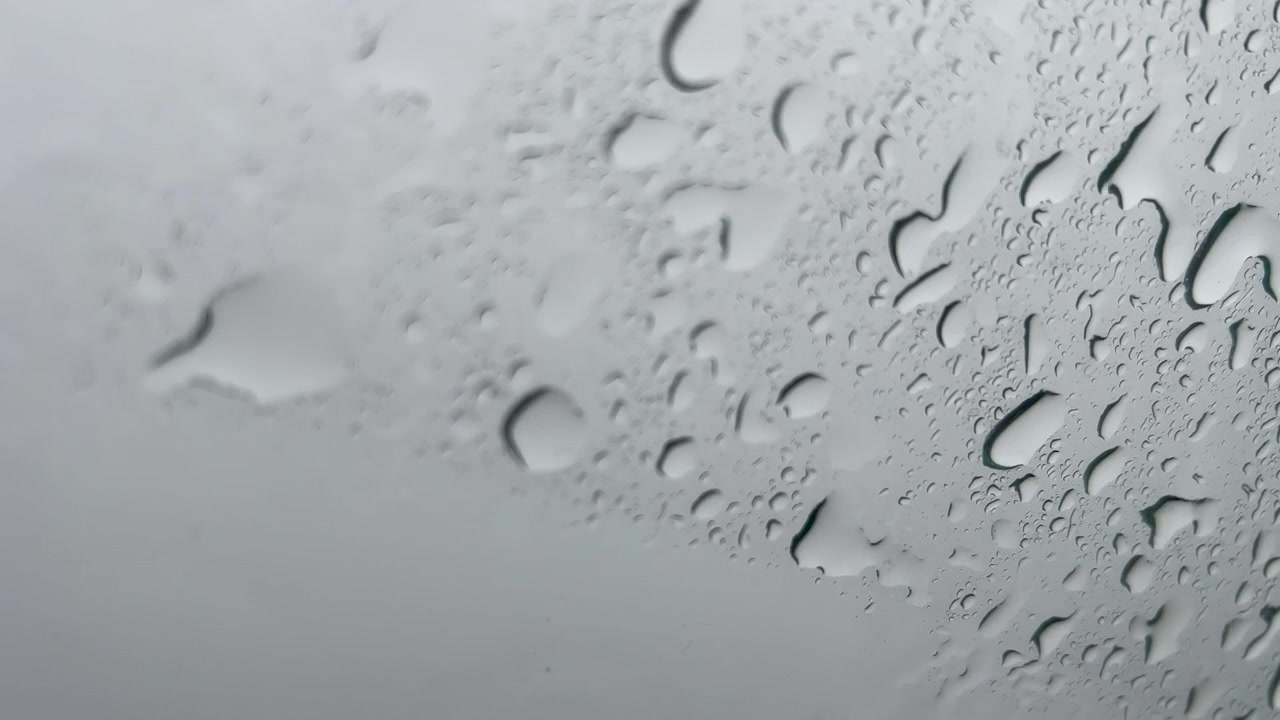 Nærbilde av vanndråper som glir ned et vindu på en regnværsdag. Filmatisk minimalistisk bakgrunn for stemnings- og værikonsepter