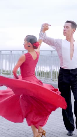 elegant couple dancing passionately in vibrant red dress and stylish attire on outdoor terrace
