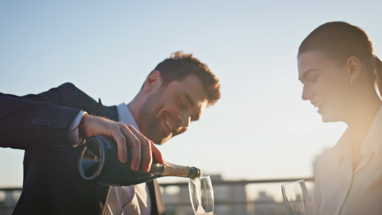 Happy businessman open champagne celebrating victory with partner on sunset roof