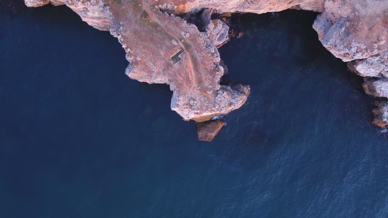 vista aérea de arriba hacia abajo de las olas salpicadas contra la costa rocosa, fondo