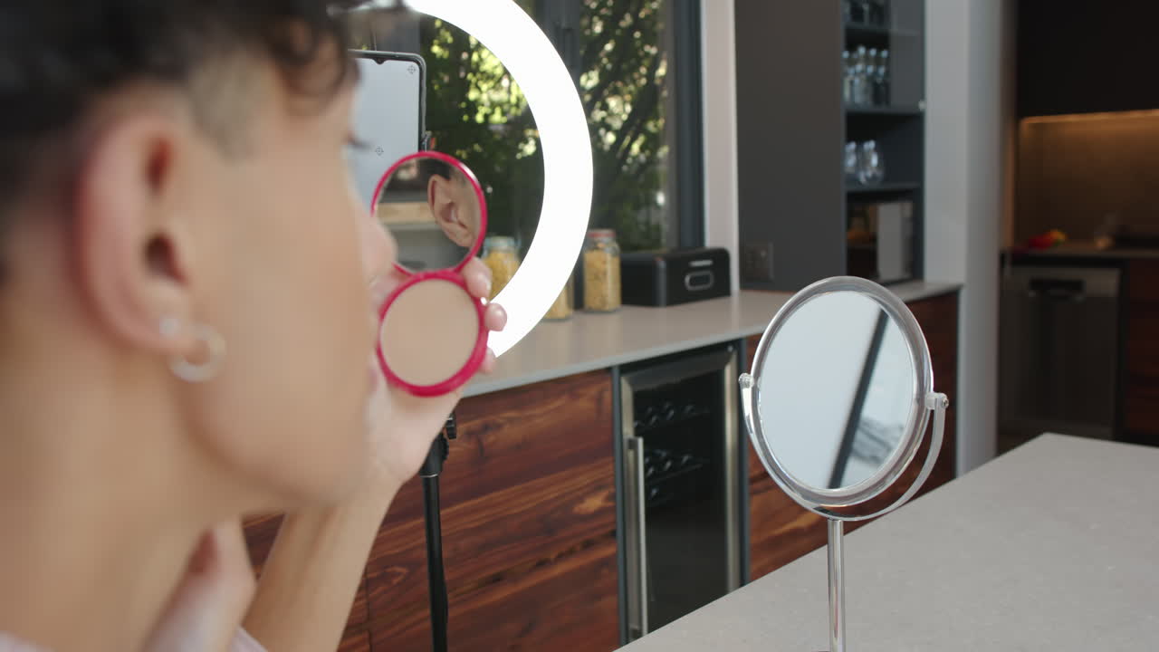 Applying makeup, person using compact mirror and ring light in modern kitchen