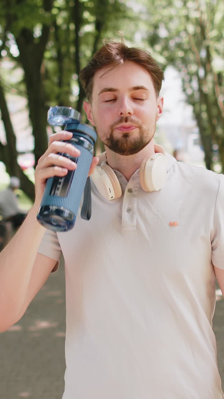 Sporty athletic thirsty man runner jogger drinking water after sport workout in park outdoors