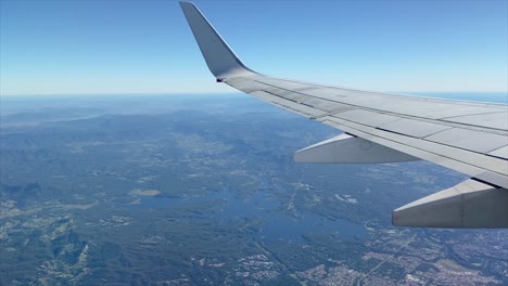 view from an airplane cruising over the state of queensland in australia, with rainforests and large lakes, distant hills, blue sky and a hazy horizon