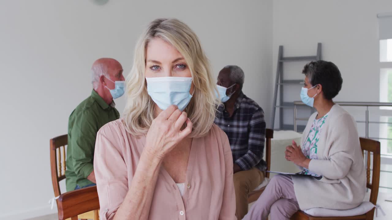 두 명의 다양한 노인 커플이 원에 앉아서 집에서 치료 대화를 나누고 카메라를 보고 있습니다.