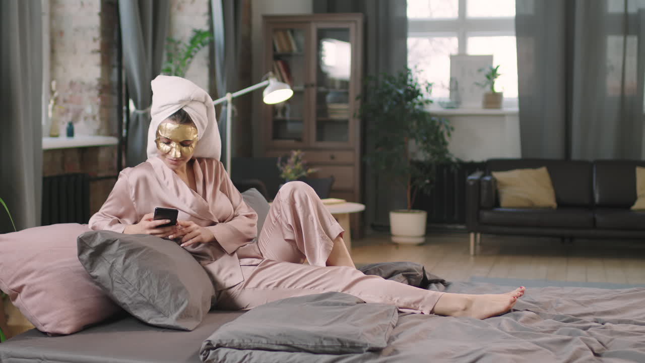 Young Woman In Gold Sheet Mask Chilling On Bed