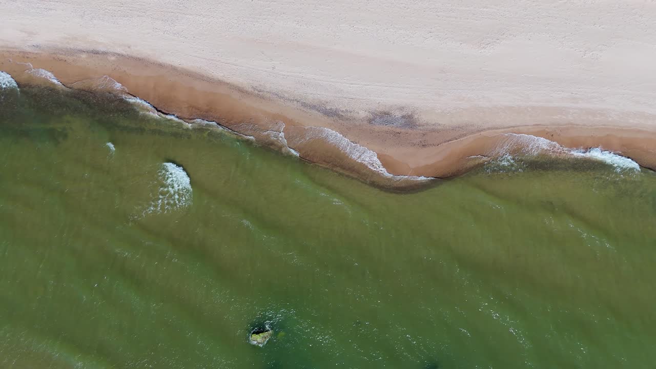 Aerial Drone Footage of Baltic Sea Waves Crashing Against Sandy Shoreline in Latvia Scenic Top-Down View of Coastal Landscape on a Bright Sunny Day with Natural Rhythmic Ocean Motion