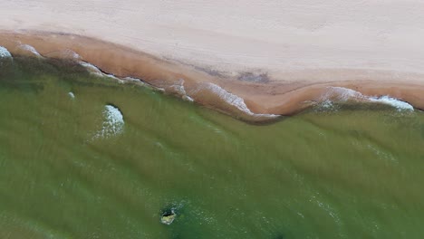 aerial drone footage of baltic sea waves crashing against sandy shoreline in latvia scenic top-down view of coastal landscape on a bright sunny day with natural rhythmic ocean motion